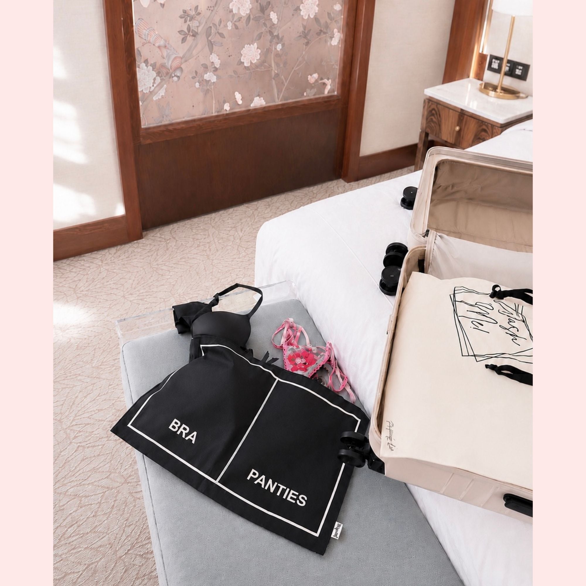 Black bags labeled 'BRA' and 'PANTIES' on a gray surface with an open suitcase in the background.