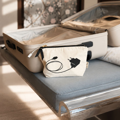 Small pouch with plug and cable design on a bed next to an open suitcase