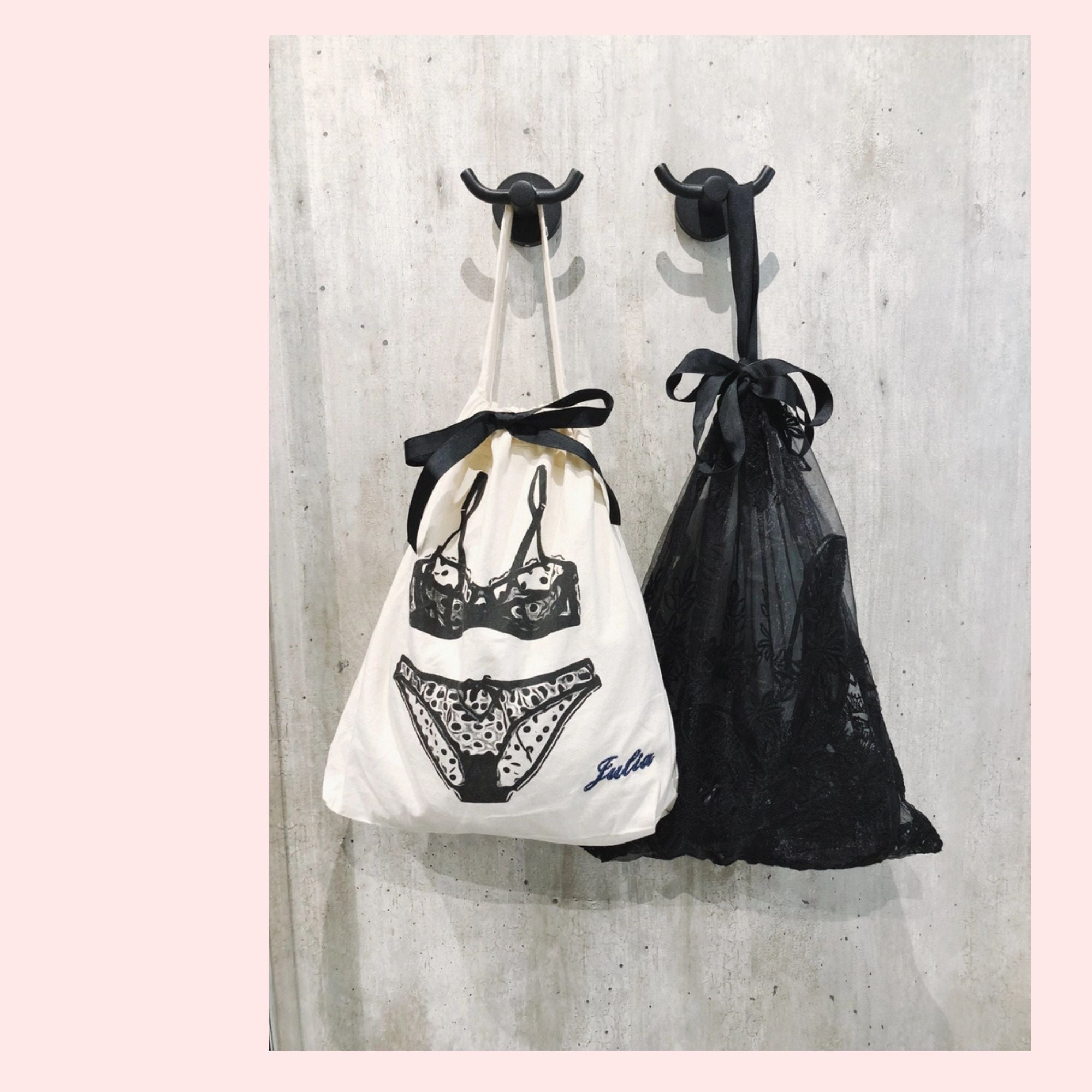 Two bags, one white with black lace design and the other black, hanging on hooks against a concrete wall.