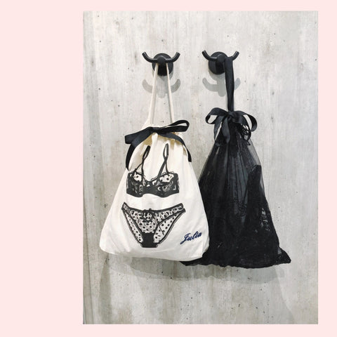 Two bags, one white with black lace design and the other black, hanging on hooks against a concrete wall.