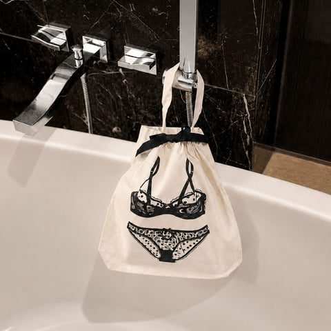 cream drawstring bag with black lingerie on a bathroom sink