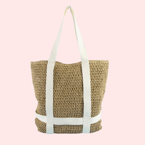 Woven straw tote bag with white straps on a pink background